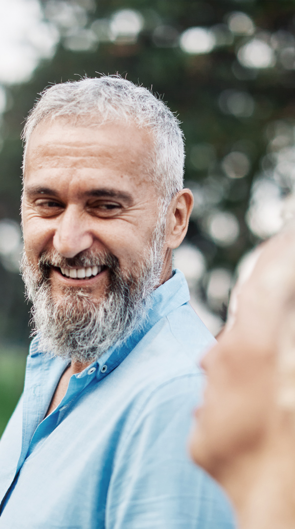 A bearded man smiling warmly while conversing outdoors, with greenery in the background in Des Moines IA. mobile