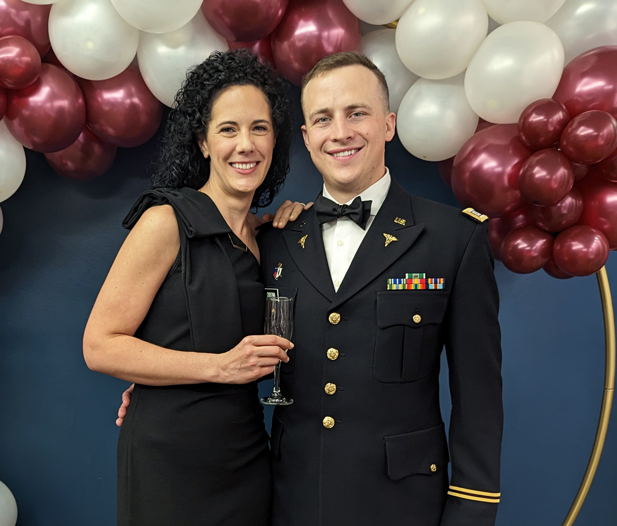 James in military uniform with woman, smiling by balloon backdrop in Des Moines IA